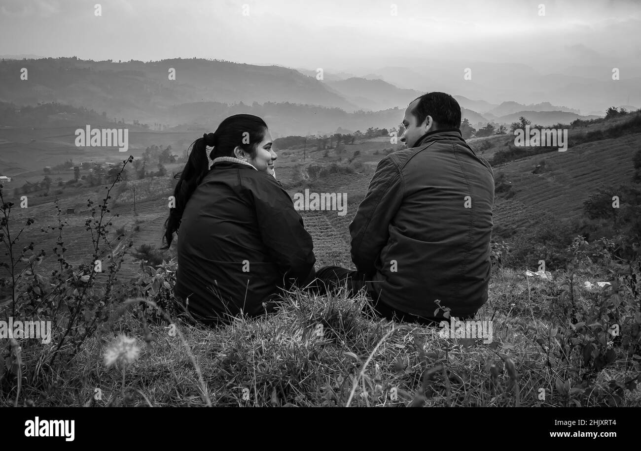 Das junge Paar, das auf der Bergspitze sitzt, mit einem nebligen Hintergrund auf der Hügelkette und einem dramatischen Himmel am Morgen in Schwarz-Weiß-Bild, wurde am Badda Peak Shil aufgenommen Stockfoto