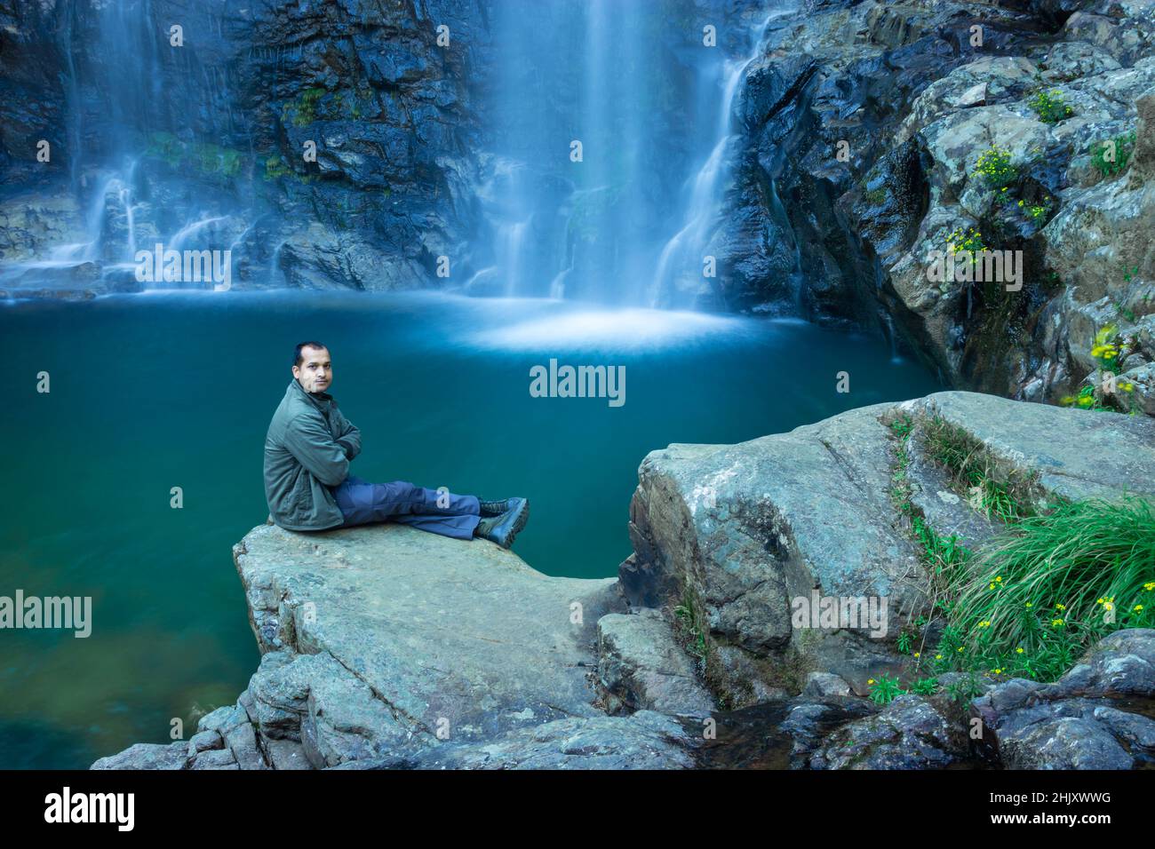 Der junge Mann am Wasserfall, der am Morgen vom Berg fällt, mit einer ruhigen, unscharfen Wasseroberfläche, wurde beim Thangsning Fall shillong meghalaya india aufgenommen. Stockfoto