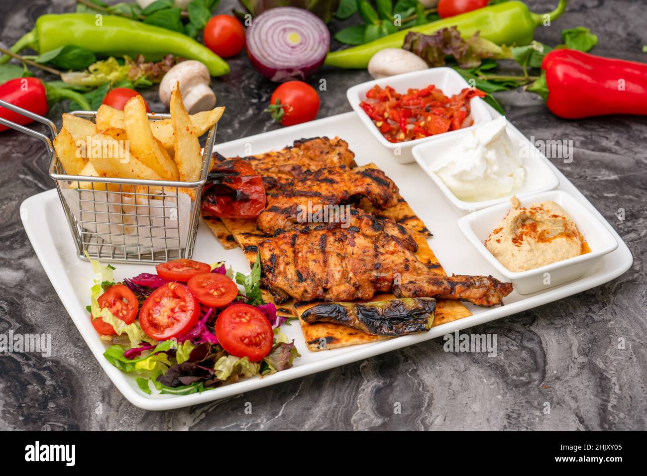 Gegrillter Hähnchenschenkel auf weißem Porzellanteller mit pommes Frites und Salat Stockfoto