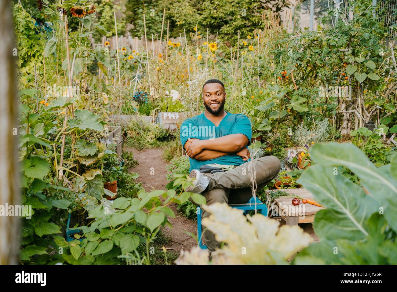 Porträt eines lächelnden Bauern mit gekreuzten Armen, der im Gemeinschaftsgarten sitzt Stockfoto