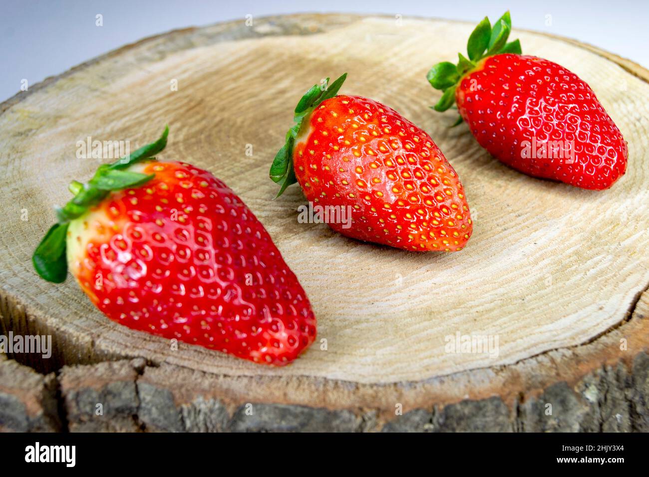 Erdbeere. Set aus drei reifen Erdbeeren auf einem braunen Holzbalken. Horizontale Fotografie. Stockfoto