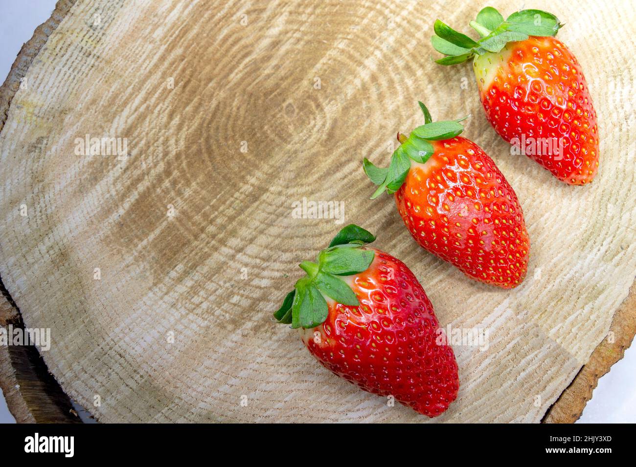 Erdbeere. Set aus drei reifen Erdbeeren auf einem braunen Holzbalken. Horizontale Fotografie. Stockfoto