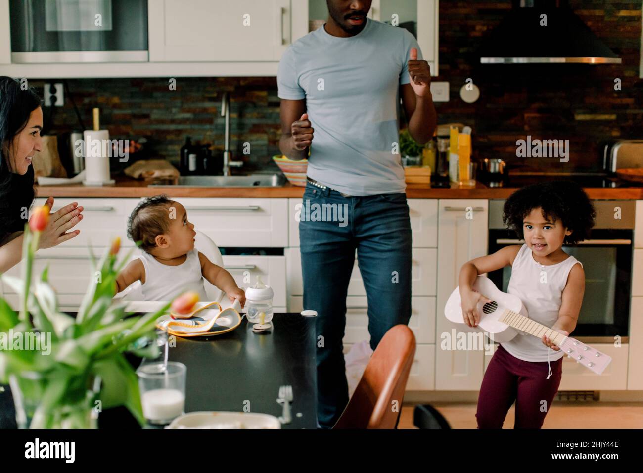 Mädchen spielt Gitarre von Familie in der Küche zu Hause Stockfoto