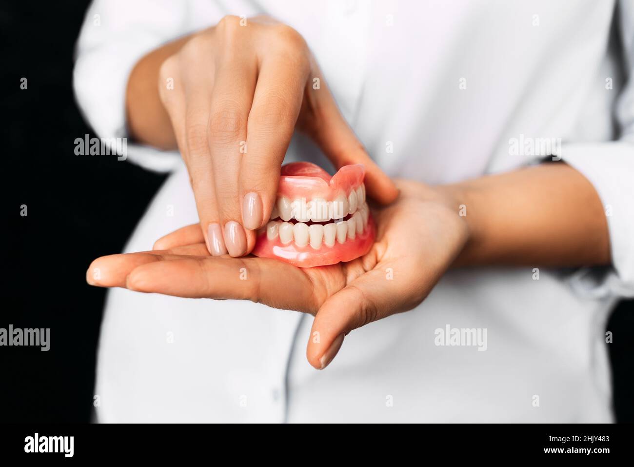 Der Zahnarzt hält Prothesen in den Händen. Zahnprothese in den Händen des Arztes Nahaufnahme. Vorderansicht der kompletten Prothese. Zahnmedizin Konzept Stockfoto