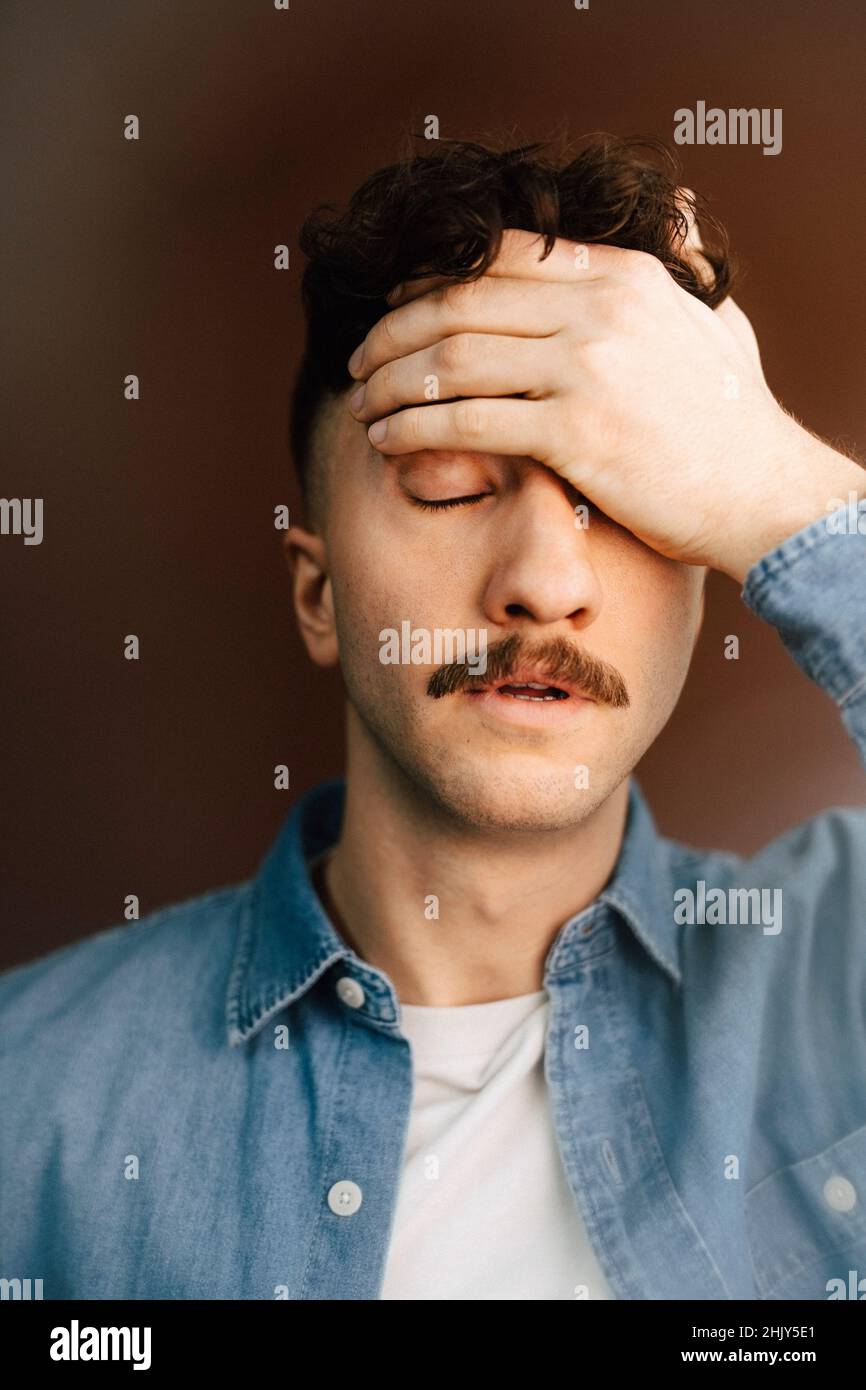 Müder junger Mann mit Kopf in der Hand vor braunem Hintergrund Stockfoto