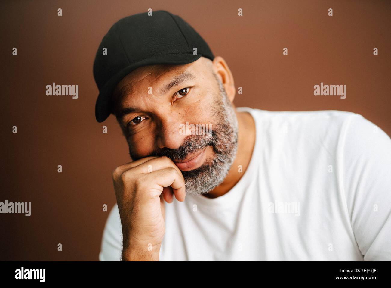 Reifer Mann mit Mütze und Hand am Kinn im Studio Stockfoto