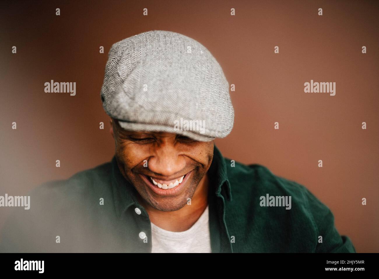 Glücklich reifer Mann trägt Baskenmütze Blick hinunter über braunen Hintergrund Stockfoto
