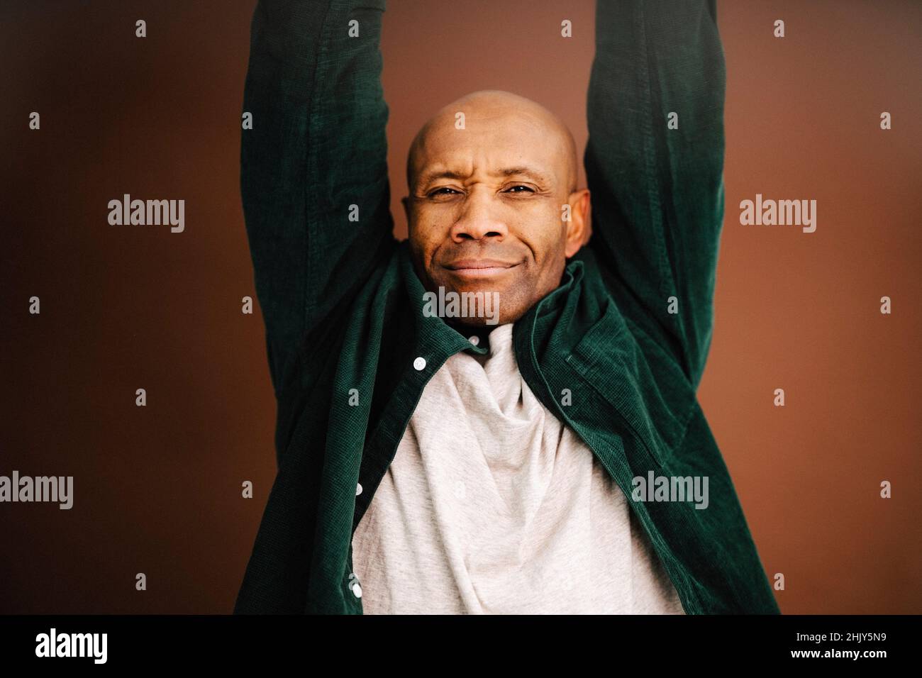 Reifer Mann mit erhobenen Armen auf braunem Hintergrund im Studio Stockfoto