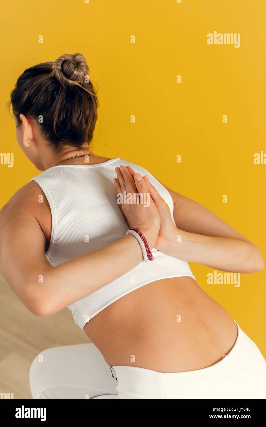 Junge Frau, die Yoga-Pose macht und ihre Hände im Gebet hinter ihrem Rücken hält. Yoga-Kurs auf gelbem Hintergrund. Das Konzept der Spiritualität und eine gesunde Stockfoto