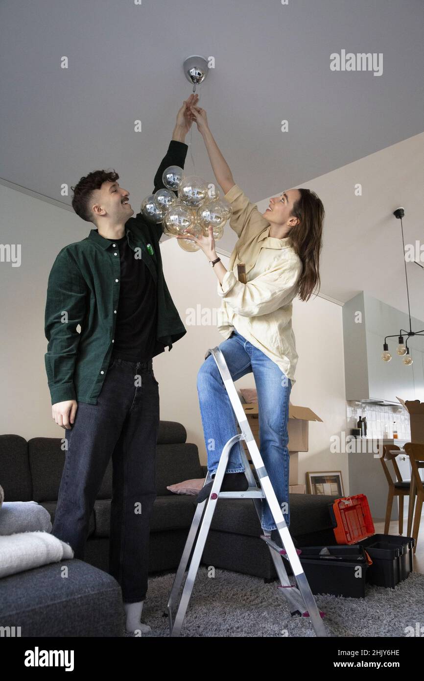 Junges Paar hängt Kronleuchter im Wohnzimmer Stockfoto