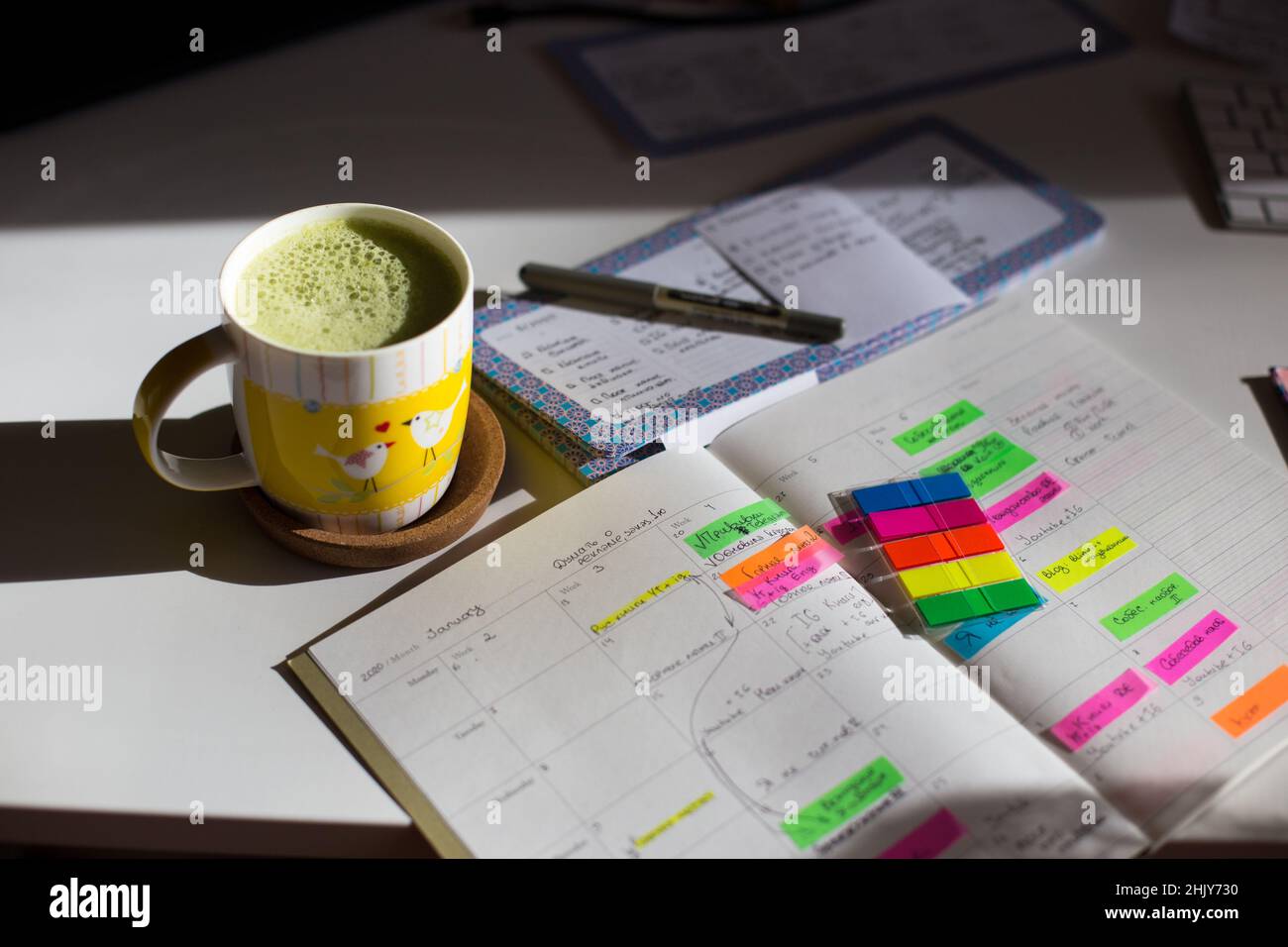 Gelbe Tasse Matcha auf dem Schreibtisch. Ein monatlicher Content-Planer in Russisch und Englisch. Hochwertige Fotos Stockfoto