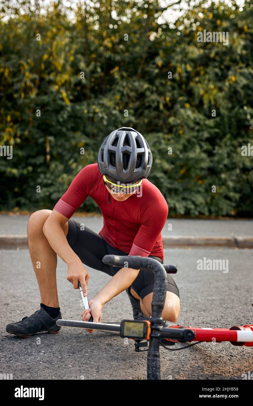 Es muss repariert werden. Athlet jungen kaukasischen Mann in sportlichen Verschleiß und Helm mit Werkzeug während der Reparatur Fahrrad im Freien, Vorbereitung auf ein Fahrrad zu fahren, enga Stockfoto