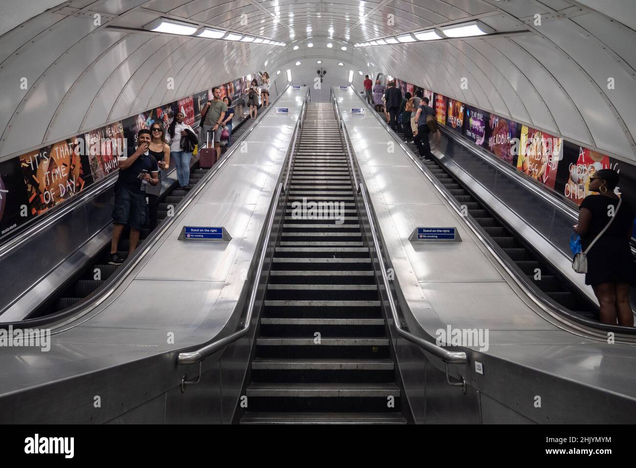 U-Bahn London. Touristen und Reisende auf den Rolltreppen des öffentlichen Nahverkehrssystems der britischen Hauptstadt. Symmetrische Architekturansicht mit niedrigem Winkel. Stockfoto
