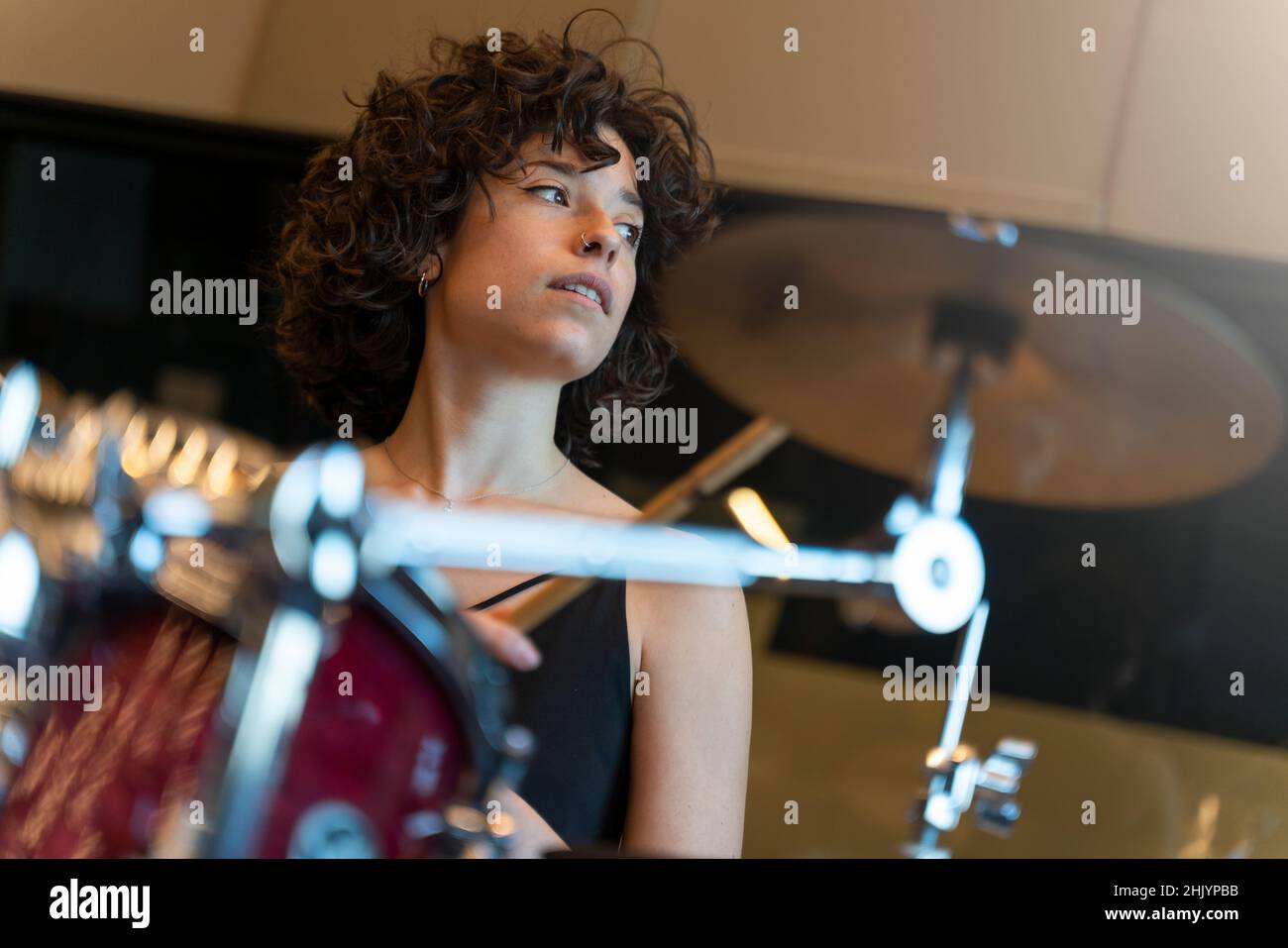 Porträt einer jungen Frau mit lockigen Haaren, die in einem Tonstudio Schlagzeug spielt Stockfoto