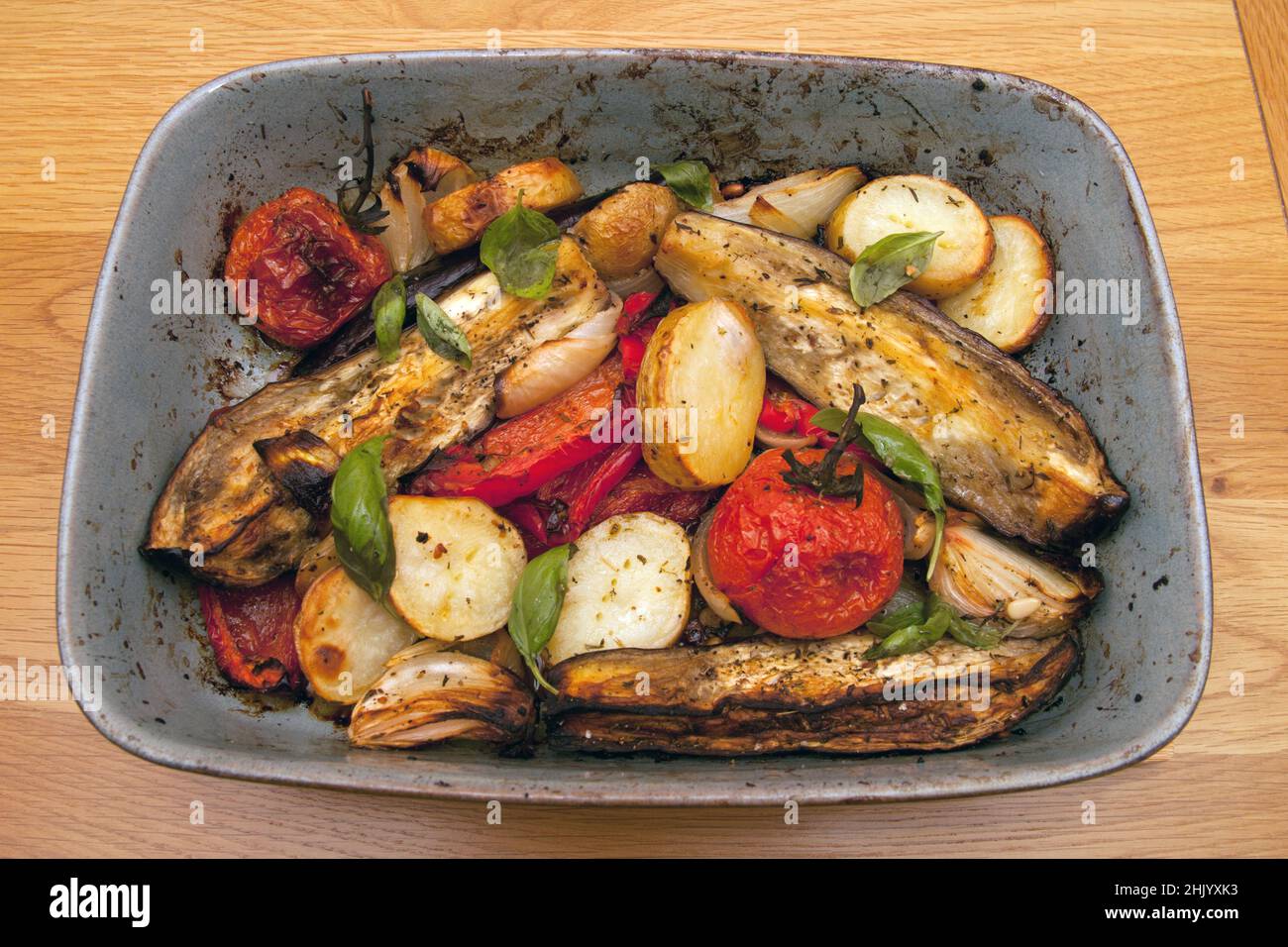 Ein Gericht mit gebratenem Gemüse, einschließlich Kartoffeln, Tomaten, Zwiebeln, Paprika und Auberginen mit frischem Basilikum Stockfoto