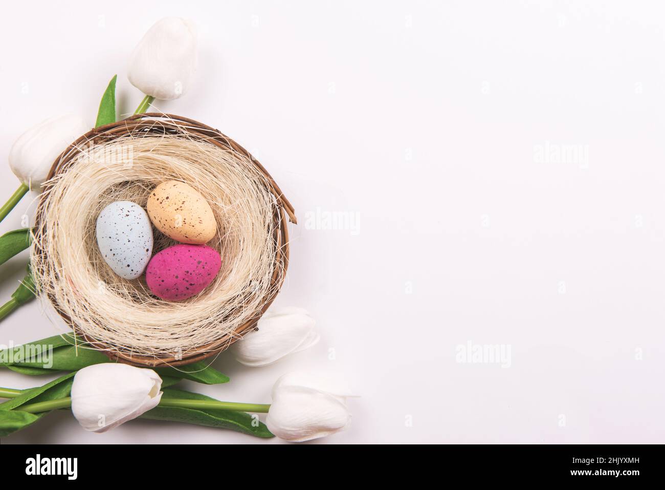 Bunte Dekorationen mit Ostereiernest und Tulpen auf weißem Hintergrund. Kopierraum, Draufsicht Stockfoto