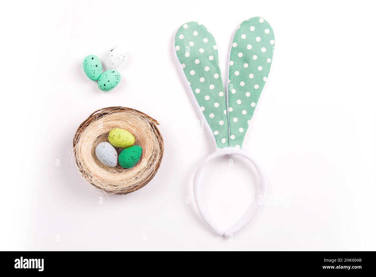 Bunte Dekorationen mit Ostereiernest und Kaninchenohren auf weißem Hintergrund. Kopierraum, Draufsicht Stockfoto