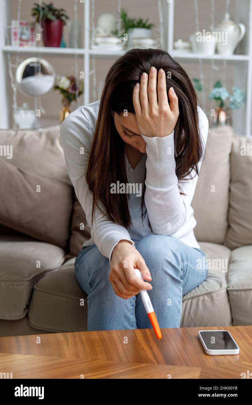 Eine traurige junge Frau hält einen Schwangerschaftstest in der Hand. Das Konzept der unerwünschten Schwangerschaft. Stockfoto