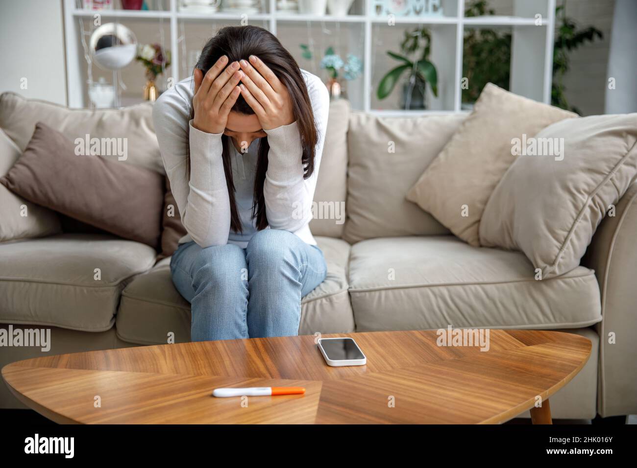 Eine traurige junge Frau hält einen Schwangerschaftstest in der Hand. Das Konzept der unerwünschten Schwangerschaft. Stockfoto
