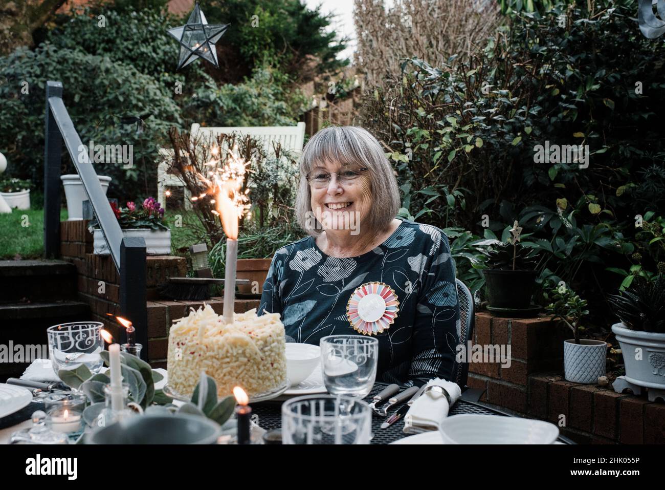 Frau saß mit einem Happy Birthday Abzeichen und Kuchen mit Wunderkerzen Stockfoto