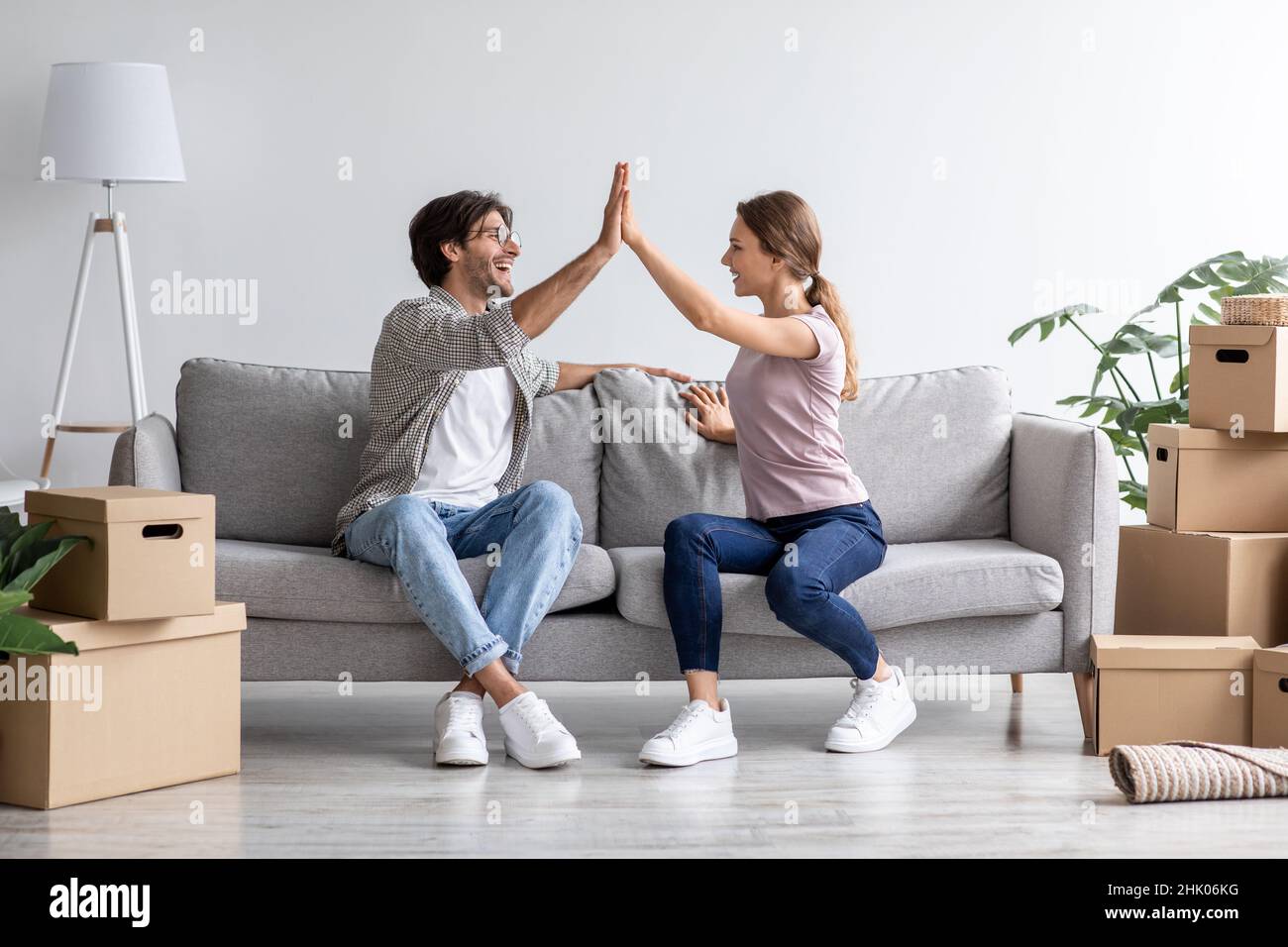 Zufriedene europäische junge Mann und Frau geben hohe fünf auf Sofa im Wohnzimmer mit Boxen Stockfoto
