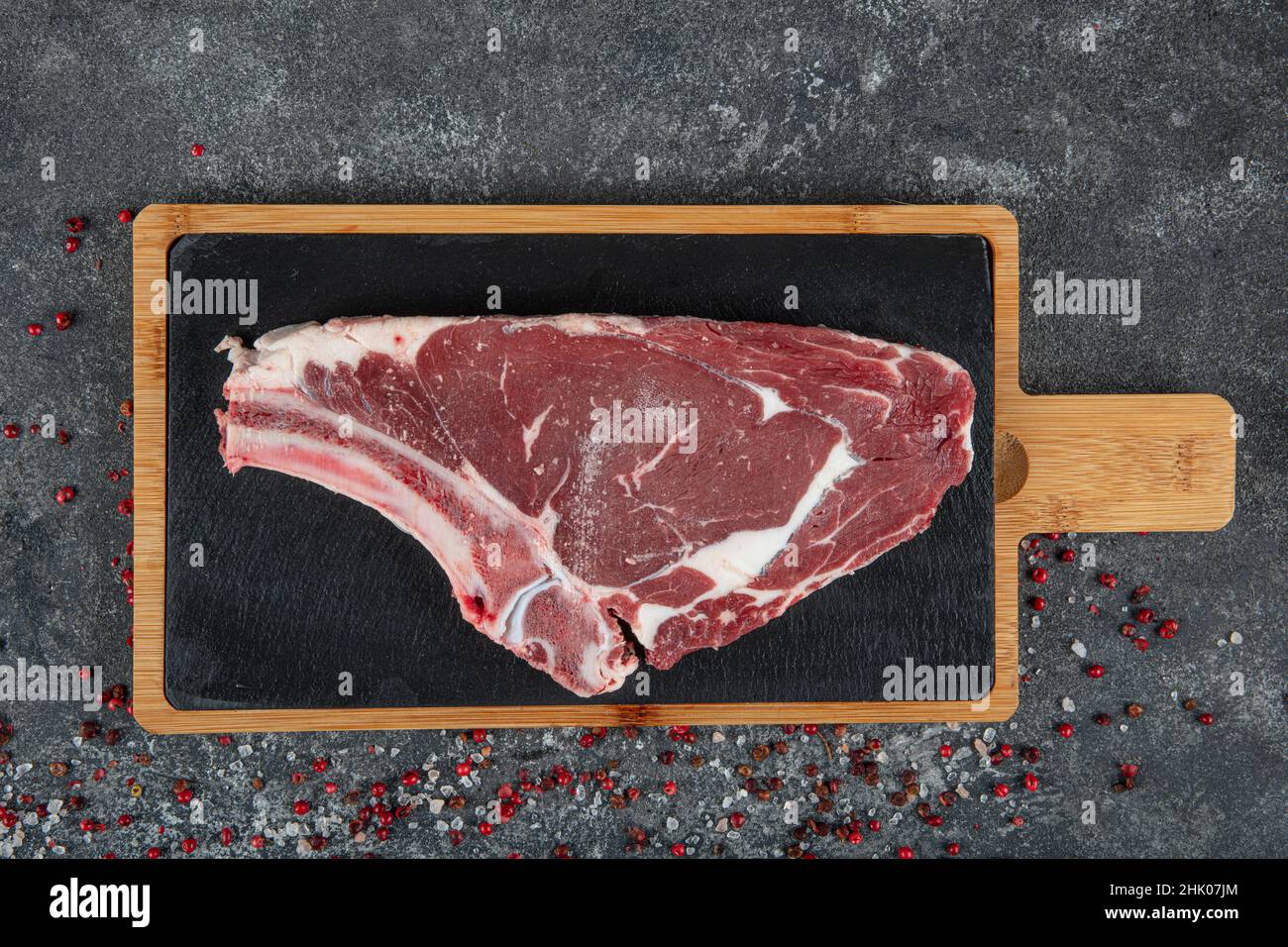 Rippchen aus frischem rohem Rindfleisch grob gehackt. Rindfleisch aus Marmor auf dem Knochenribeye. Rohes Cowboy-Steak mit Gewürzen auf steinernem Hintergrund, Prime Rib Eye on Bone, Stockfoto