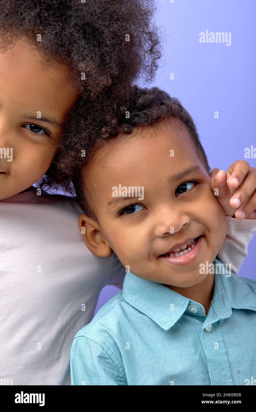 Zwei glückliche schwarze Kinder posieren vor der Kamera und fröhlich lächeln über lila Studio Hintergrund, niedlich amerikanischen Bruder und Schwester Spaß zusammen, Stockfoto