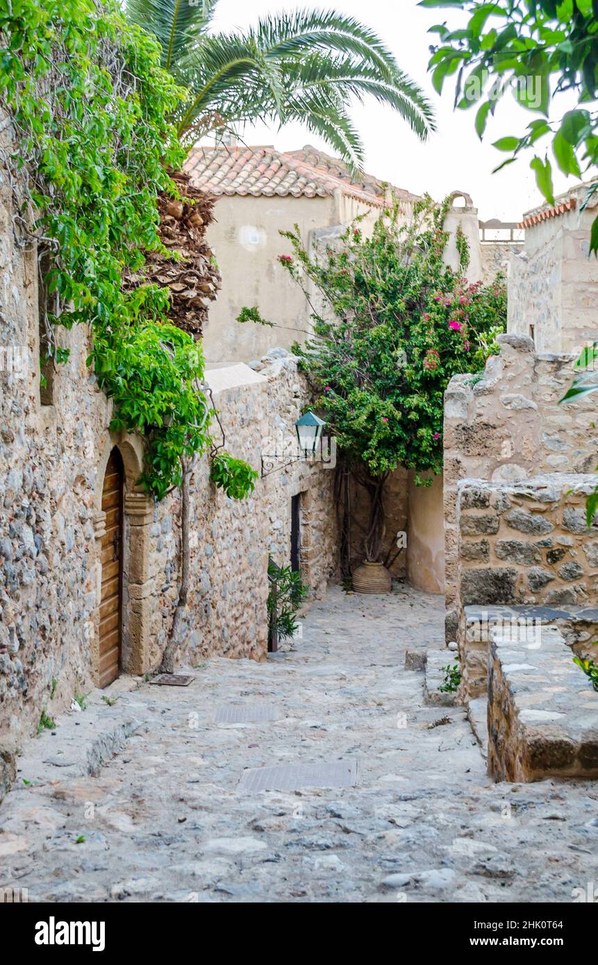 Schöne traditionelle mittelalterliche Straße auf der Insel Monemvasia, Peloponnes, Griechenland. Byzantinische Allee mit Steinhaus-Eingängen, Bäumen und Pflanzen. Stockfoto