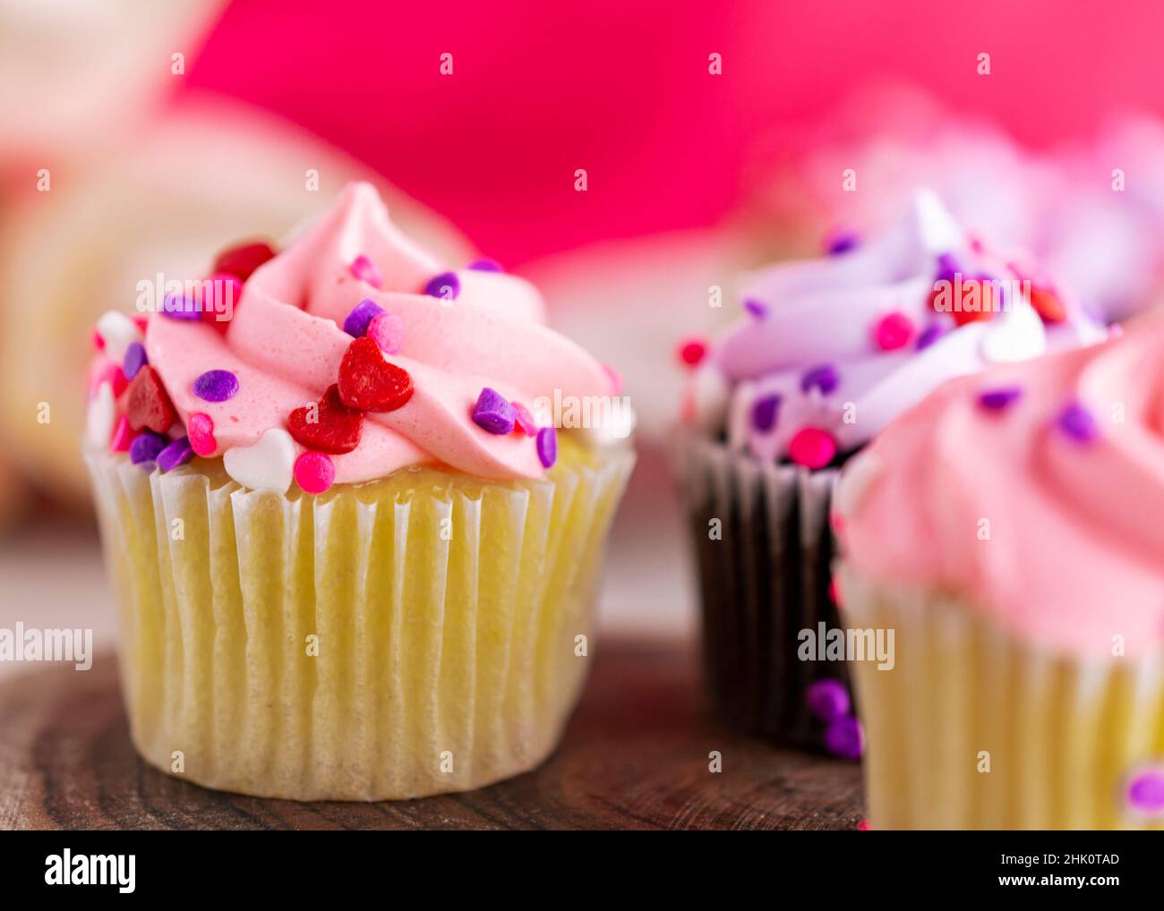 Eine Nahaufnahme einer Auswahl an kleinen Valentinstag-Cupcakes auf einer Holzplatte. Rosa Hintergrund mit einer sehr geringen Schärfentiefe. Stockfoto