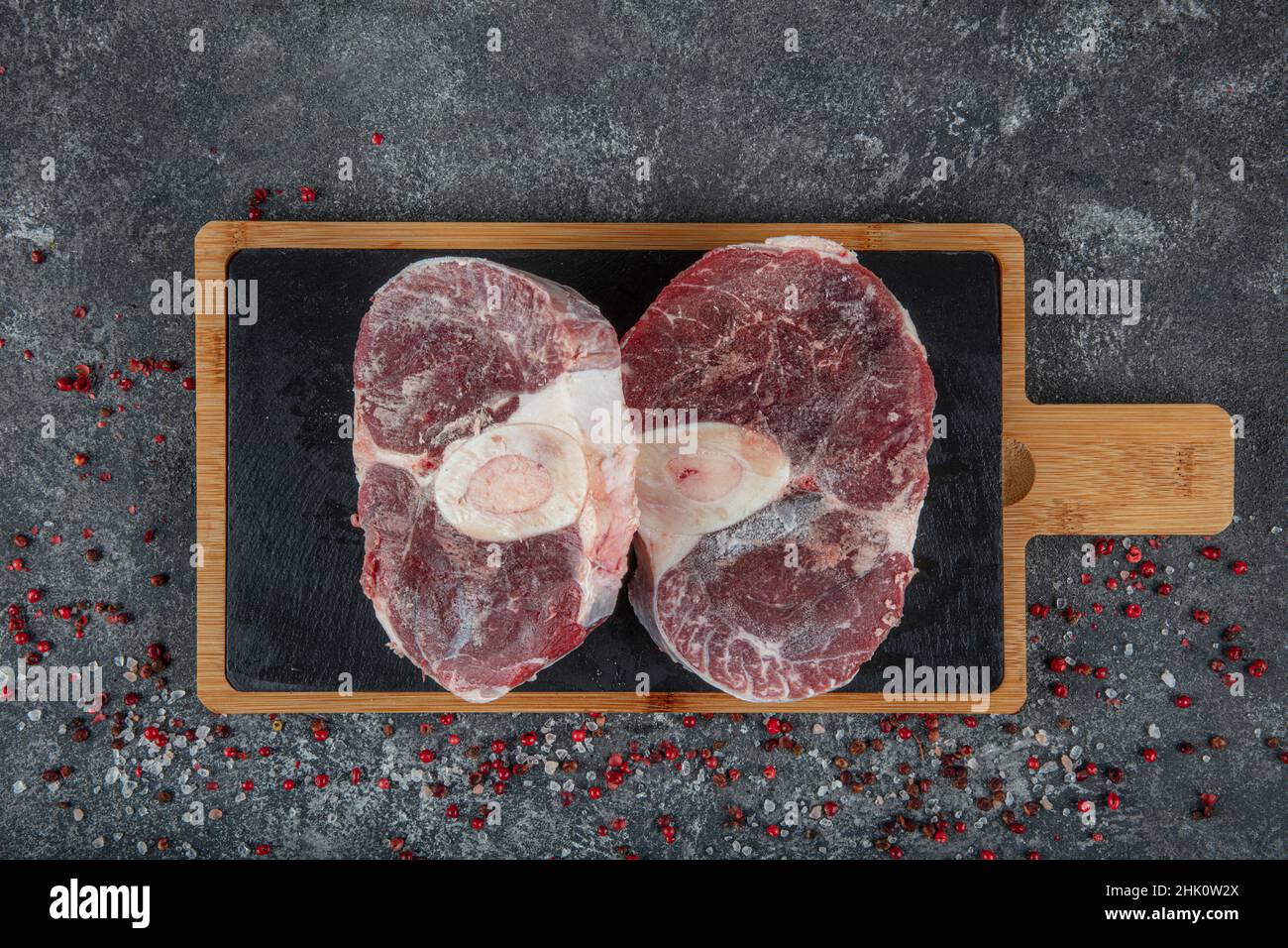 Rippchen aus frischem rohem Rindfleisch grob gehackt. Rindfleisch aus Marmor auf dem Knochenribeye. Rohes Cowboy-Steak mit Gewürzen auf steinernem Hintergrund, Prime Rib Eye on Bone, Stockfoto