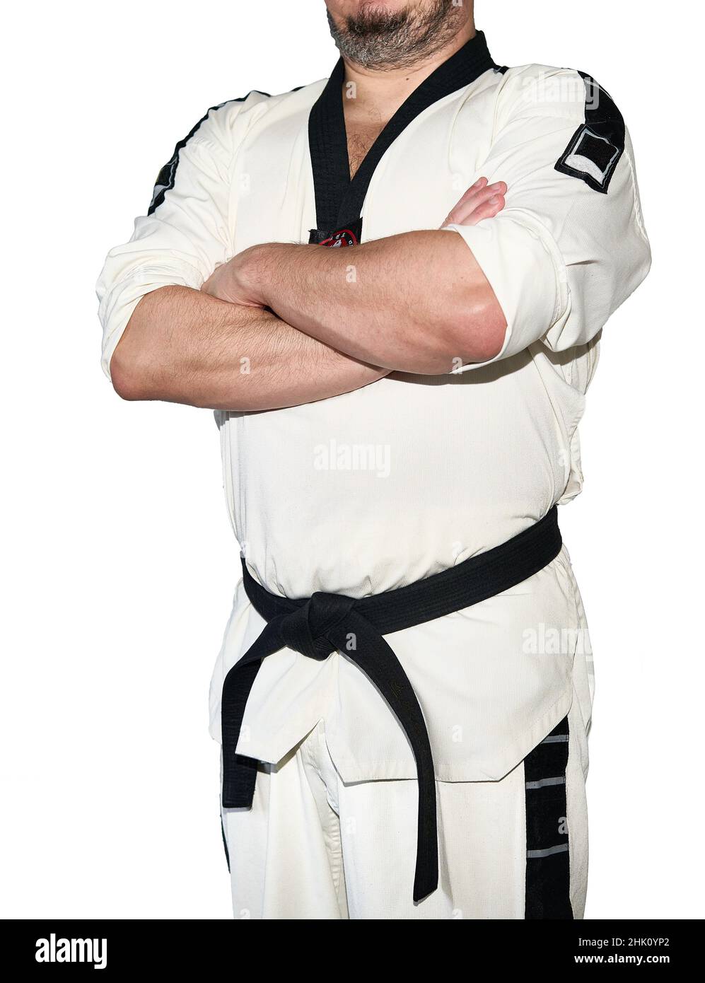 Mann in Taekwondo-Kampfkunstuniform faltet seine Arme isoliert auf dem weißen Hintergrund. Schwarzer Gürtel Stockfoto