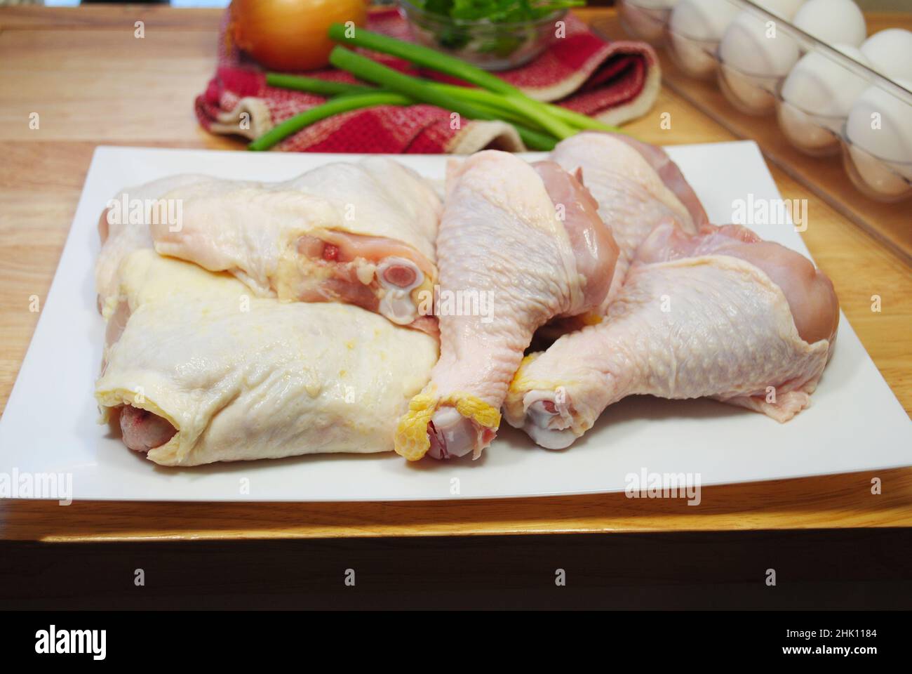 Rohe Hähnchenbeine und Oberschenkel auf einem Teller mit frischen Zutaten im Hintergrund Stockfoto