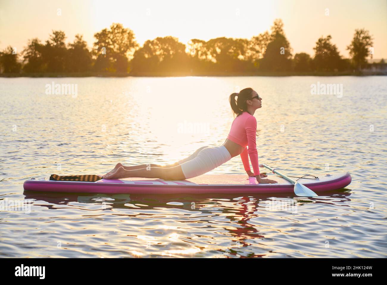 Schöne aktive Frau macht Fitness-Übungen auf supboard mit erstaunlichen Sommer Sonnenuntergang auf dem Hintergrund. Wassersport und Menschen Konzept. Stockfoto