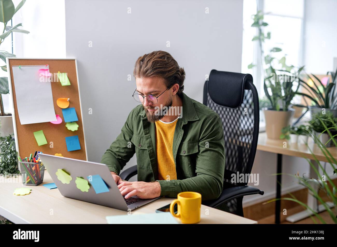 Angenehme kaukasische Mann sitzen allein im Büro hinter dem Schreibtisch arbeiten online auf Laptop, Eingabe auf der Tastatur. Schöner Kerl in Freizeitkleidung konzentriert und Focu Stockfoto