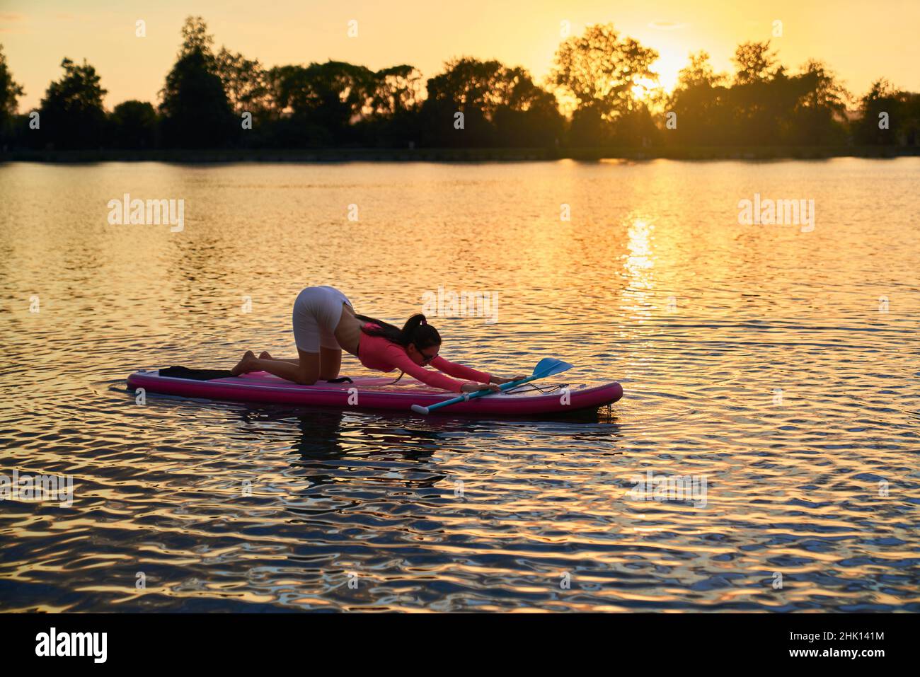 Schlanke junge Frau in activewear Stretching Körper auf supboard während schönen Sommer Sonnenuntergang. Konzept von Menschen, Ausgleich und Wasseraktivität. Stockfoto