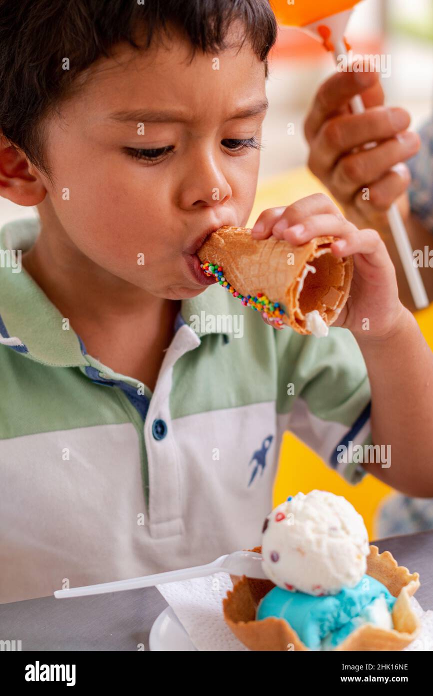 Lateinisches Kind, das auf lustige Weise ein Eis isst. Eis mit Keksen für Kinder Stockfoto