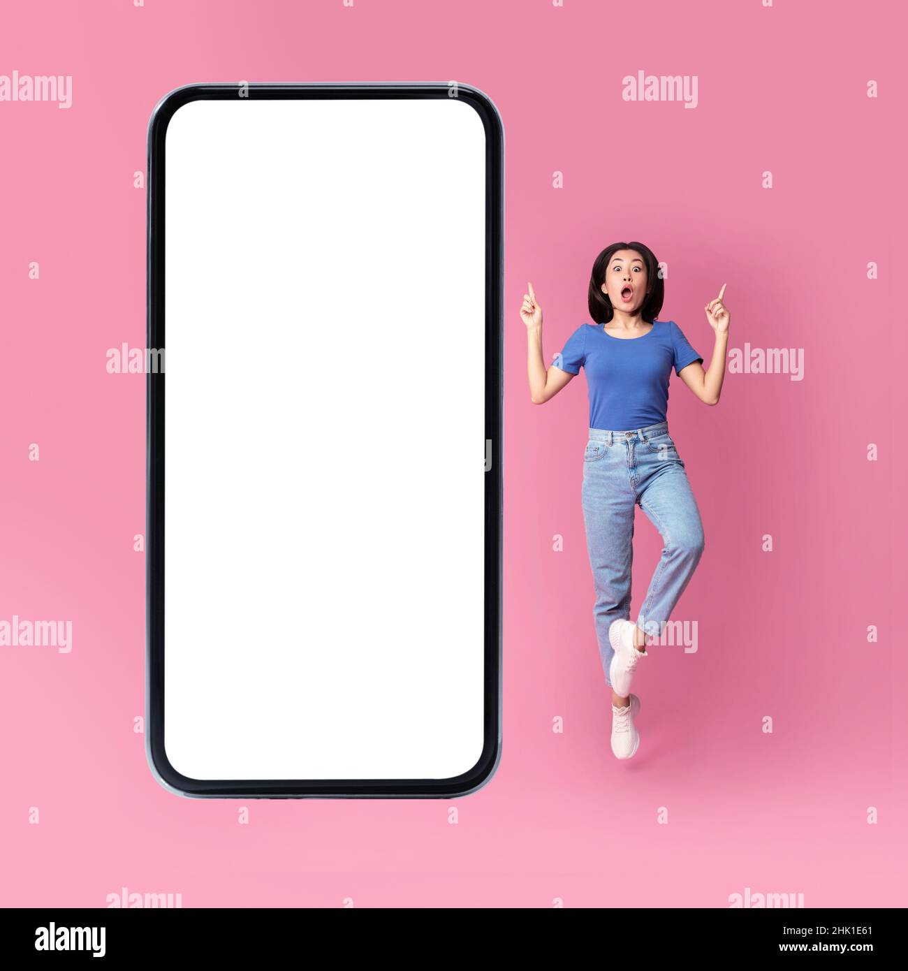 Überrascht Asiatische Dame Springen In Der Nähe Von Riesigen Handy-Bildschirm, Rosa Hintergrund Stockfoto