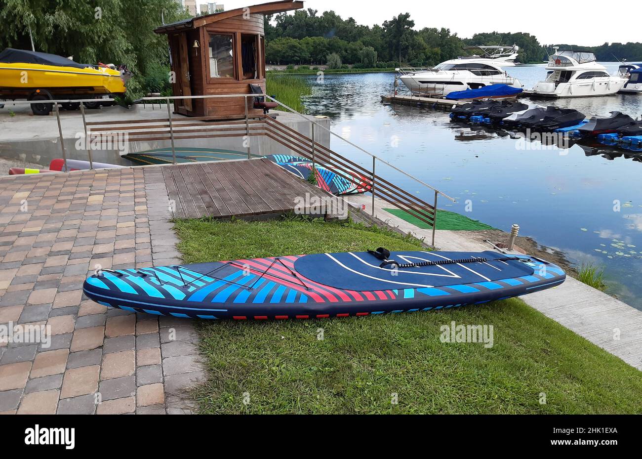 Im Vordergrund ruht ein knallfarbenes SUP-Paddel auf einem Dock. Motorroller und Motorboote im Hintergrund Stockfoto