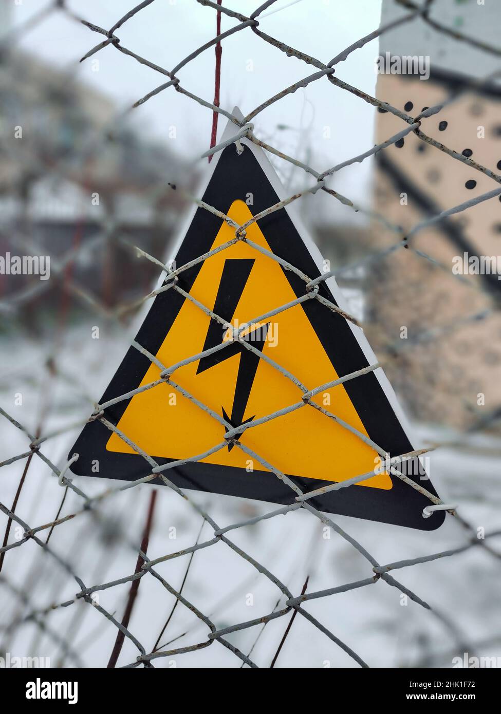 Ein dreieckiges Warnschild hängt an einem Drahtzaun über gefährliche hohe elektrische Spannung dahinter. Stockfoto