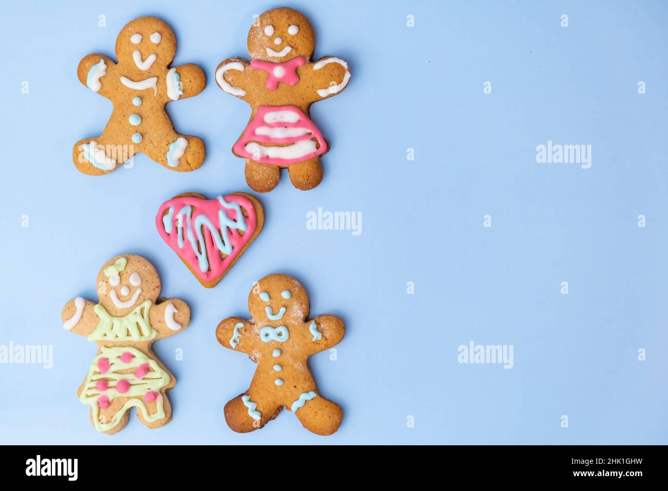 Heterosexuelle Plätzchenpaare, Jungen und Mädchen und Lebkuchenherz mit Glasur auf dem blauen Hintergrund mit Kopierraum. Kekse zum Valentinstag Stockfoto