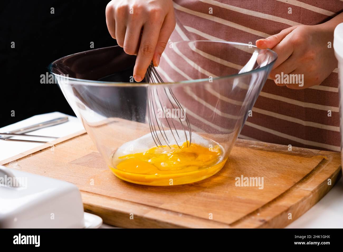 Nahaufnahme der Hände einer Frau, die Eier schlagen, um Teig auf dem Holztisch in der Küche zu machen. Hausgemachte Küche. Stockfoto