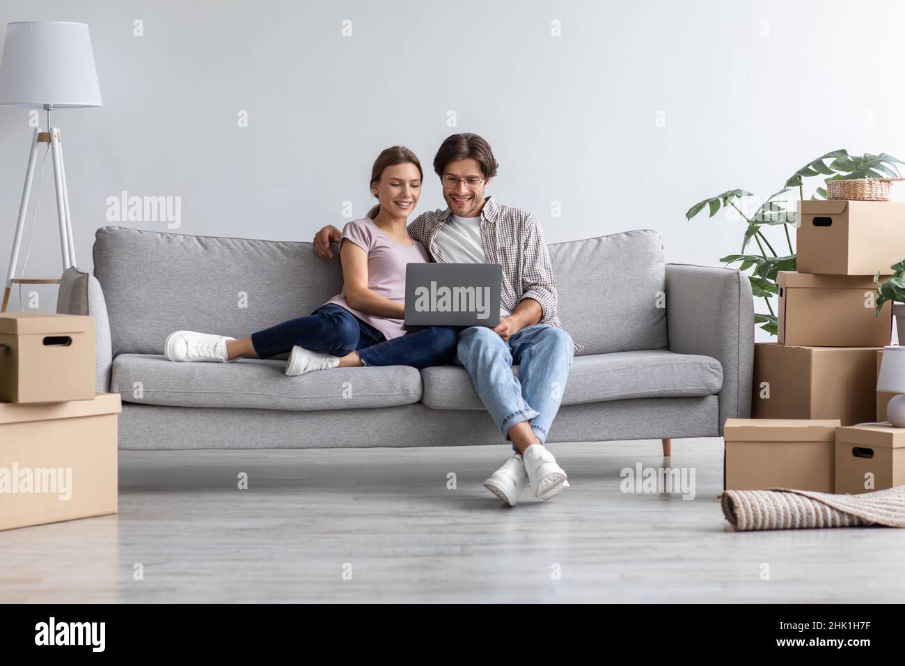 Beschäftigt glücklich europäischen jungen Mann zeigen Computer für die Frau auf dem Sofa im Wohnzimmer Interieur Stockfoto