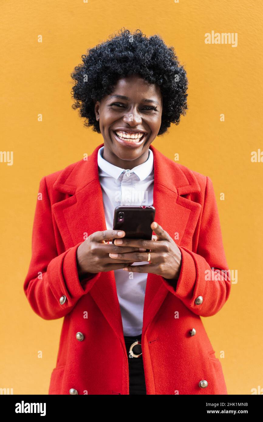 Afroamerikanische Frau, die die Kamera ansah und lachte, während sie ein Mobiltelefon hielt. Stockfoto