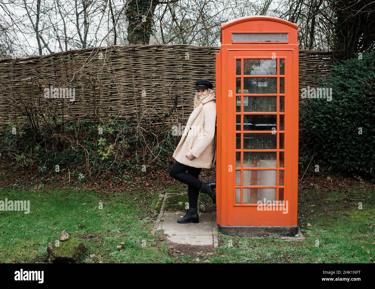 Frau, die sich an einen traditionellen englischen Telefonkasten lehnt Stockfoto