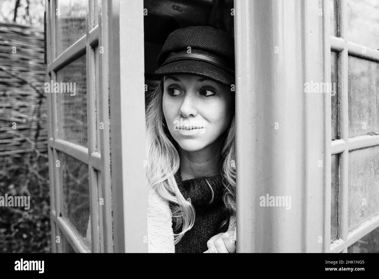 Schwarz-Weiß-Porträt einer Frau, die aus einer englischen Telefonbox schaut Stockfoto