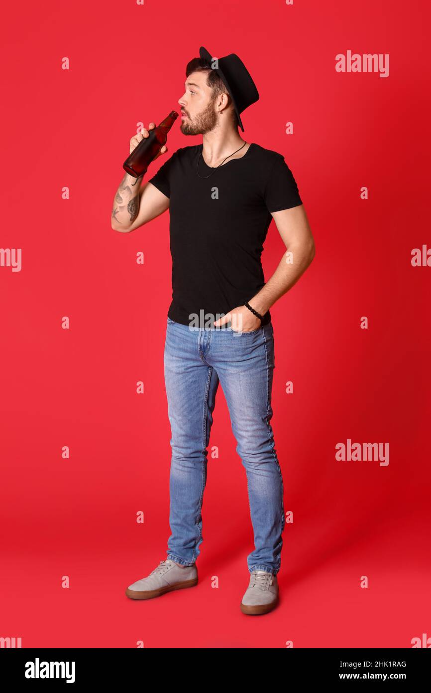 Stilvoller junger Mann, der Bier auf rotem Hintergrund trinkt Stockfoto