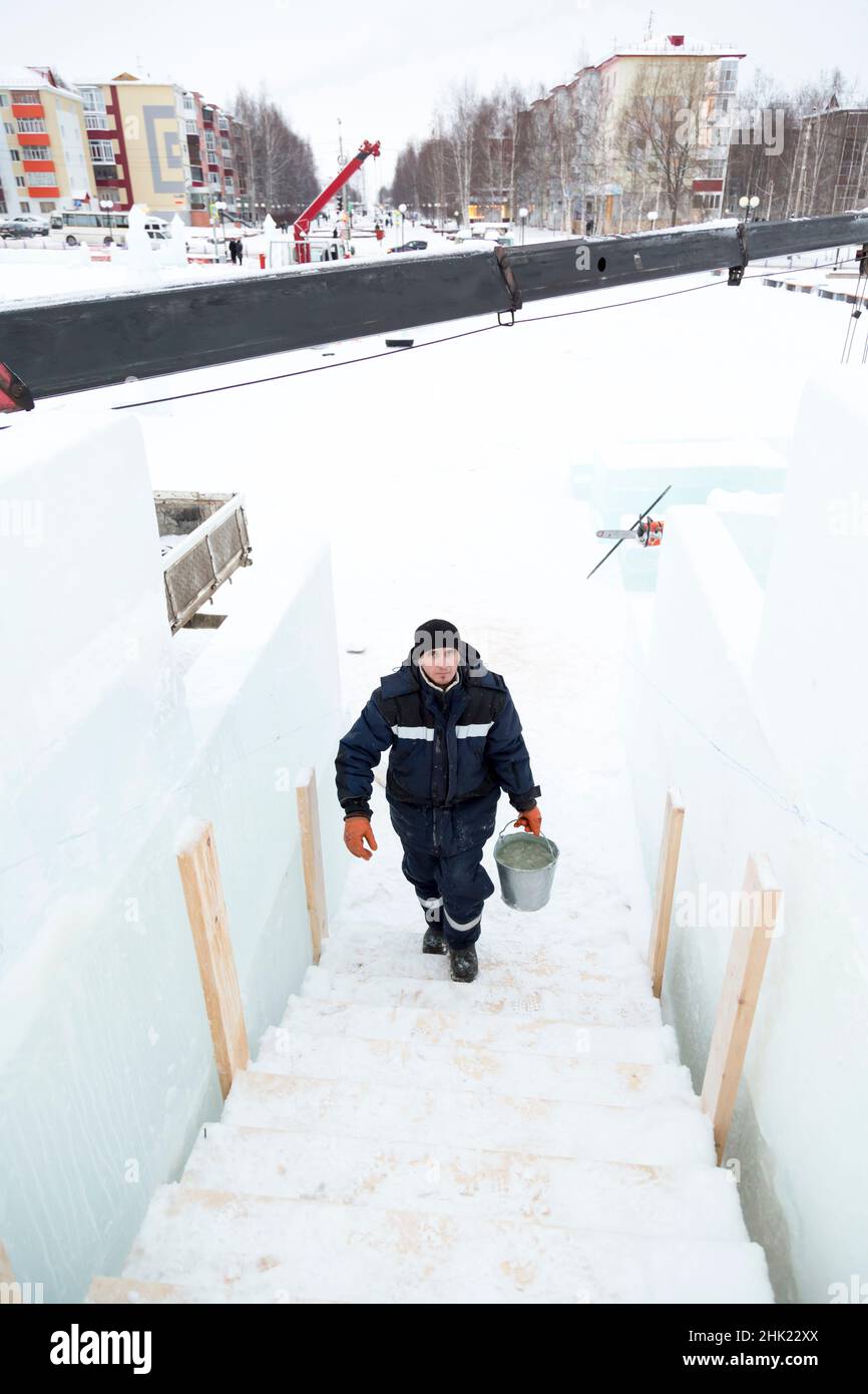 Ein Arbeiter in einer blauen Jacke und einem schwarzen Hut geht die Treppe mit einem Eimer Schnee hinauf Stockfoto