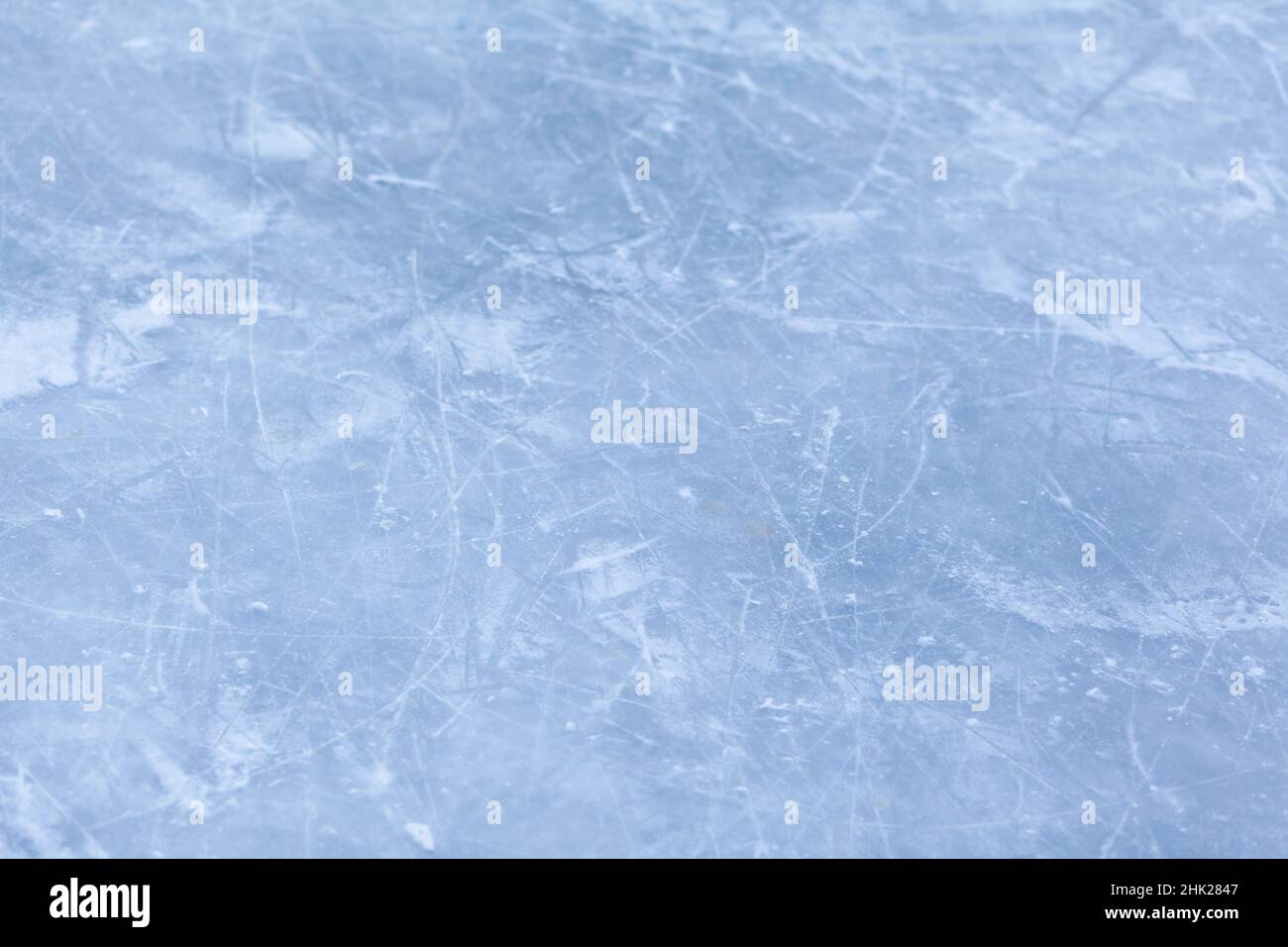 Leere Eisbahn mit Schlittschuhspuren nach der Sitzung im Freien. Eislaufbahn Textur mit Schnee bei Tageslicht bedeckt. Nahaufnahme von blauem Eislaufboden, CO Stockfoto