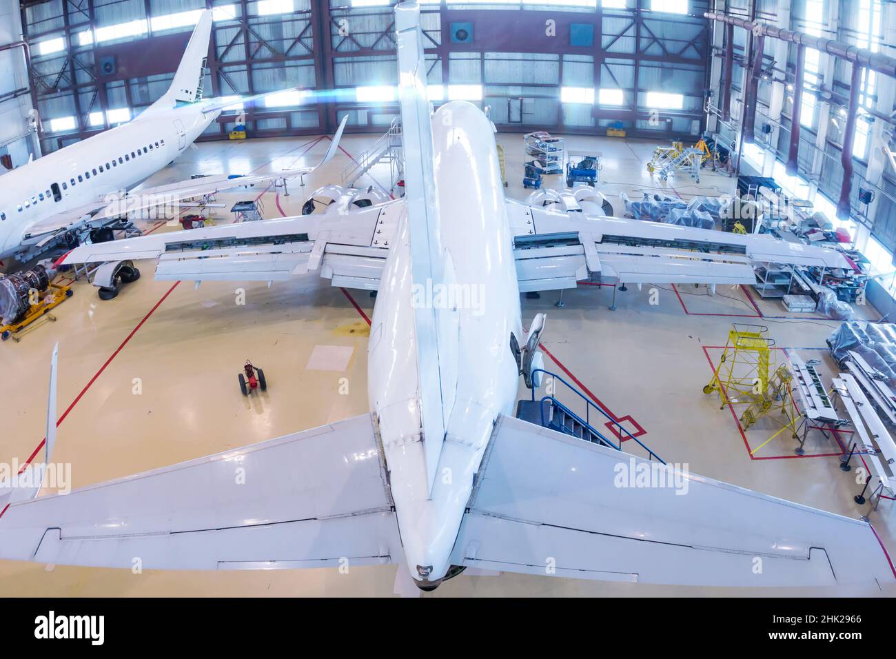 Draufsicht auf ein weißes Passagierflugzeugin im Hangar. Flugzeuge, die in Wartung sind. Überprüfung der mechanischen Systeme für den Flugbetrieb Stockfoto