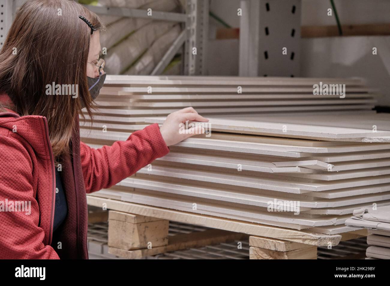 Frau in Maske gegen Virus kauft Faserplatten im Baustofflager Stockfoto